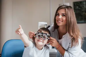 A woman optometrist is helping a child wear an eyeglass for an eye test in an office