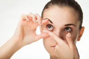 Close up of a woman inserting a contact lens into her eye.