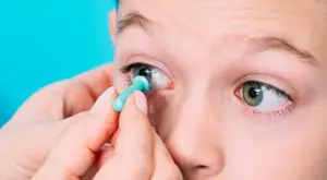 A close up of a child putting in a contact lens with a blue background