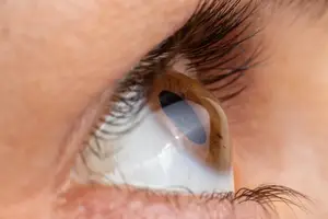 A close-up of a human eye with a brown iris and white sclera, surrounded by eyelashes, captured in a studio setting.