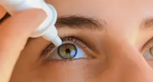 A close-up of a woman's eye with a person applying eye drops.