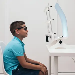 A boy in a blue shirt and glasses sits at a table with a vision testing device.