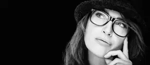 Woman with glasses and hat thinking, with hand on chin