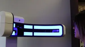 A woman with glasses is looking at a futuristic device that has a blue and white LED light display mounted on a wall.