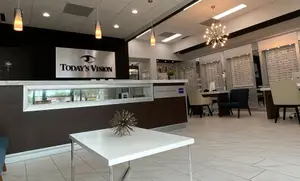 A white desk with a decorative object in front of a reception counter with the text Today’s Vision at the top in an optical shop.