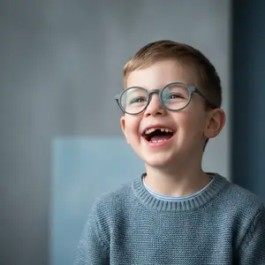 Young boy wearing glasses and smiling in front of a blue wall
