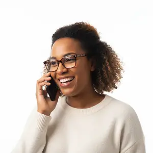 A smiling woman wearing glasses and a white sweater is talking on her phone against a white background.