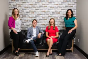 Four people are sitting on a couch with brick wall in the background.
