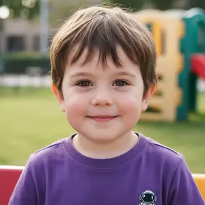 A close-up of a little boy wearing a purple t-shirt with an astronaut print on it, smiling and posing for a photo at a playground.