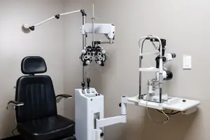 An image of an optometrist's office with a black leather chair and an eye examination machine mounted on the wall