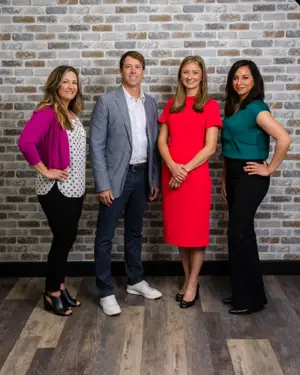Four people posing for a photo in front of a brick wall