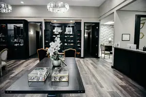 A well-decorated room with a table and chairs, a cabinet with shelves, a chandelier, and a frame on the wall.