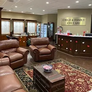 A room with leather couches, a wooden coffee table, and a counter with a sign reading 'Child & Family Eye Care'.
