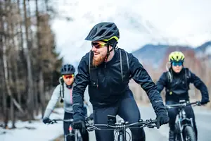 Three people riding bicycles on a snowy mountain road, with the man in the middle wearing a helmet and sunglasses, and the others wearing helmets as well.