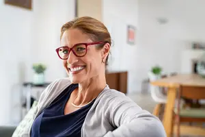Woman wearing glasses smiling and sitting on a couch in a room