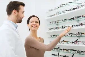 A woman looking at glasses with a man in a white lab coat in front of her