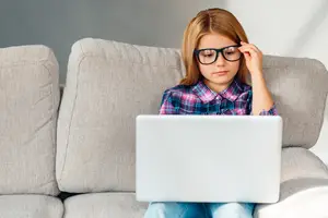 A girl sitting on a couch while using a laptop
