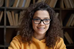 Curly-haired girl with glasses smiling in front of a bookshelf
