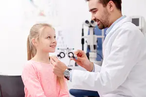 A young girl with glasses is smiling at the doctor while he is examining her eyes.
