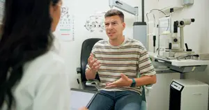 man sitting in chair at optometrists office talking to woman