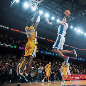 Two basketball players are jumping and trying to dunk a basketball in a basketball arena.