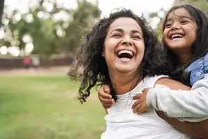 A woman and a young girl are laughing and having fun in a park on a sunny day.