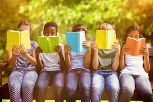 Five children sitting on a bench while reading books in an outdoor area