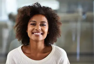 African American woman with curly hair and white top smiling in an office setting