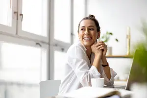 A woman sitting at a desk with a laptop and cup smiling for the camera