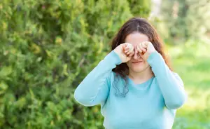 A woman standing outdoors covering her eyes with her hands