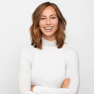 A smiling woman with short hair and a white turtleneck top is standing and posing for a picture.