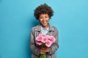 Happy woman in a gray jacket holding a bouquet of pink gerbera daisies.