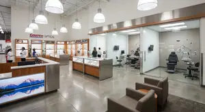 An inside look at a Costco Optical store, featuring a reception desk, chairs, and medical equipment in a glass-walled examination room.