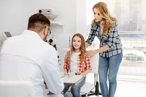 A doctor examining a young girl's eyes in an examination room