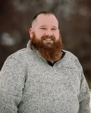 a man with a beard and a gray sweater smiling at the camera
