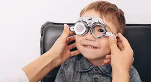 A child wearing glasses is being examined by a doctor or optometrist