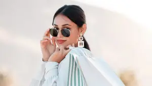A woman in sunglasses and earrings holding a white and green striped shopping bag