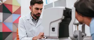 A male doctor is checking the eye of a woman using a medical device