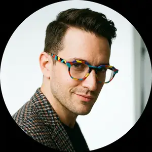 A smiling man wearing colorful glasses and a patterned jacket