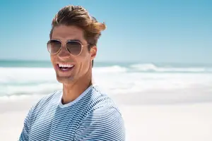 A man in sunglasses smiles at the camera on a beach