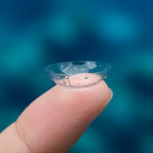 A person holding a clear contact lens on their fingertip.