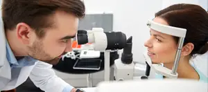 A man and a woman are examining the woman's eyes using an ophthalmoscope.