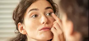 woman putting in a contact lens in front of a mirror