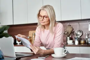 A woman is sitting in the kitchen and reading a document on her laptop
