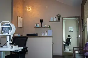 An indoor space with a desk, chairs, and various items, including a lamp, monitor, and potted plant, is depicted in this image.