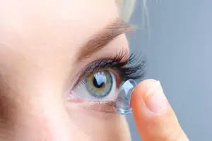 A woman is putting a contact lens into her eye.