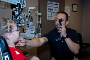 An adult male is examining a child's eyes with an ophthalmoscope in an examination room