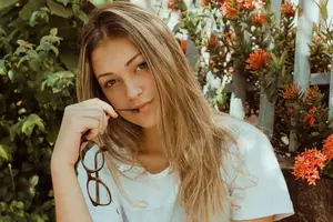 A woman with long hair is smiling and holding a pair of glasses in her hand.
