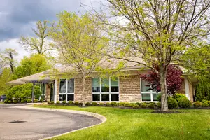 A house with glass windows, a driveway, and lush green grass under a cloudy sky.