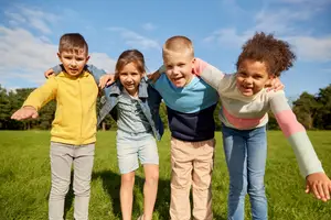 Four kids standing in a grassy field under a cloudy sky.